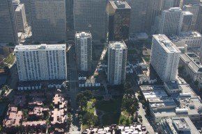 High-angle view of a city with many tall buildings. A park sits in the center with trees and walkways.