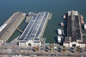 Aerial view of a pier with solar panels, docked boats, and palm trees along the waterfront.