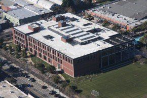 Aerial view of a brick building with a flat roof, large windows, and a grassy area in front.