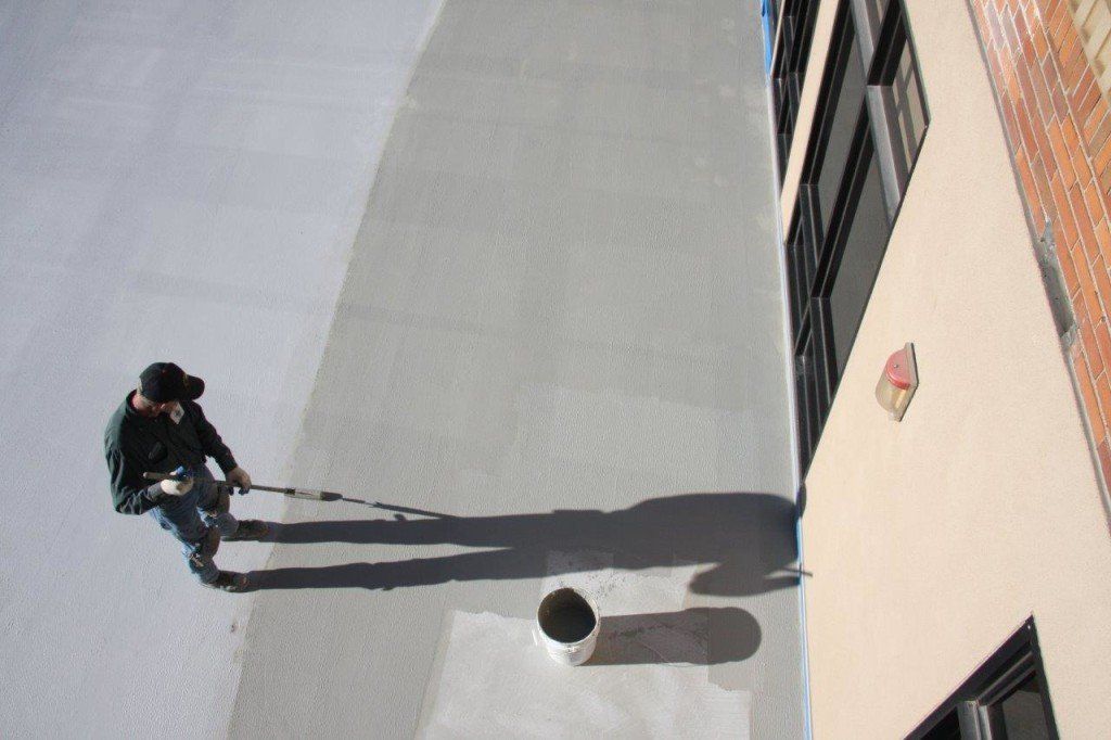 A person painting a wall on a building's exterior with a roller; a long shadow is cast.