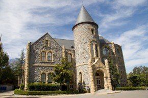 Stone building with tower, arched entry, and gray roof against blue sky.