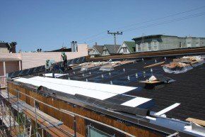 Workers installing solar panels on a rooftop. Bright sunlight. Buildings in the background.