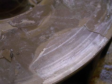 Nahaufnahme einer beschädigten Metalloberfläche mit Rissen und weißen Streifen, wahrscheinlich Abnutzungsspuren.