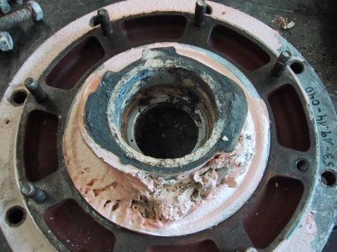 Beschädigtes Industriebauteil mit rosa und schwarzem Dichtmittel um ein zentrales Loch.