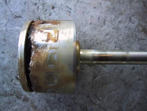 Ein korrodierter Metallzylinder ist an einer Metallstange befestigt und ruht auf einer grauen Oberfläche.