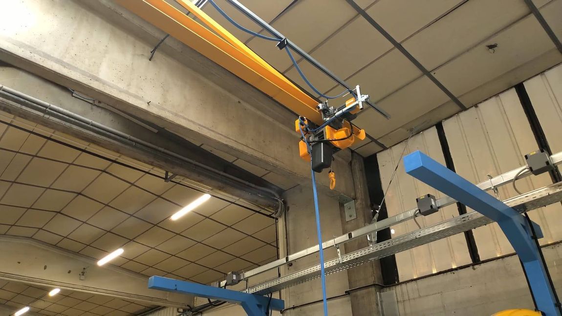 Braccio robotico industriale montato a soffitto in un magazzino, sopra una struttura metallica blu.