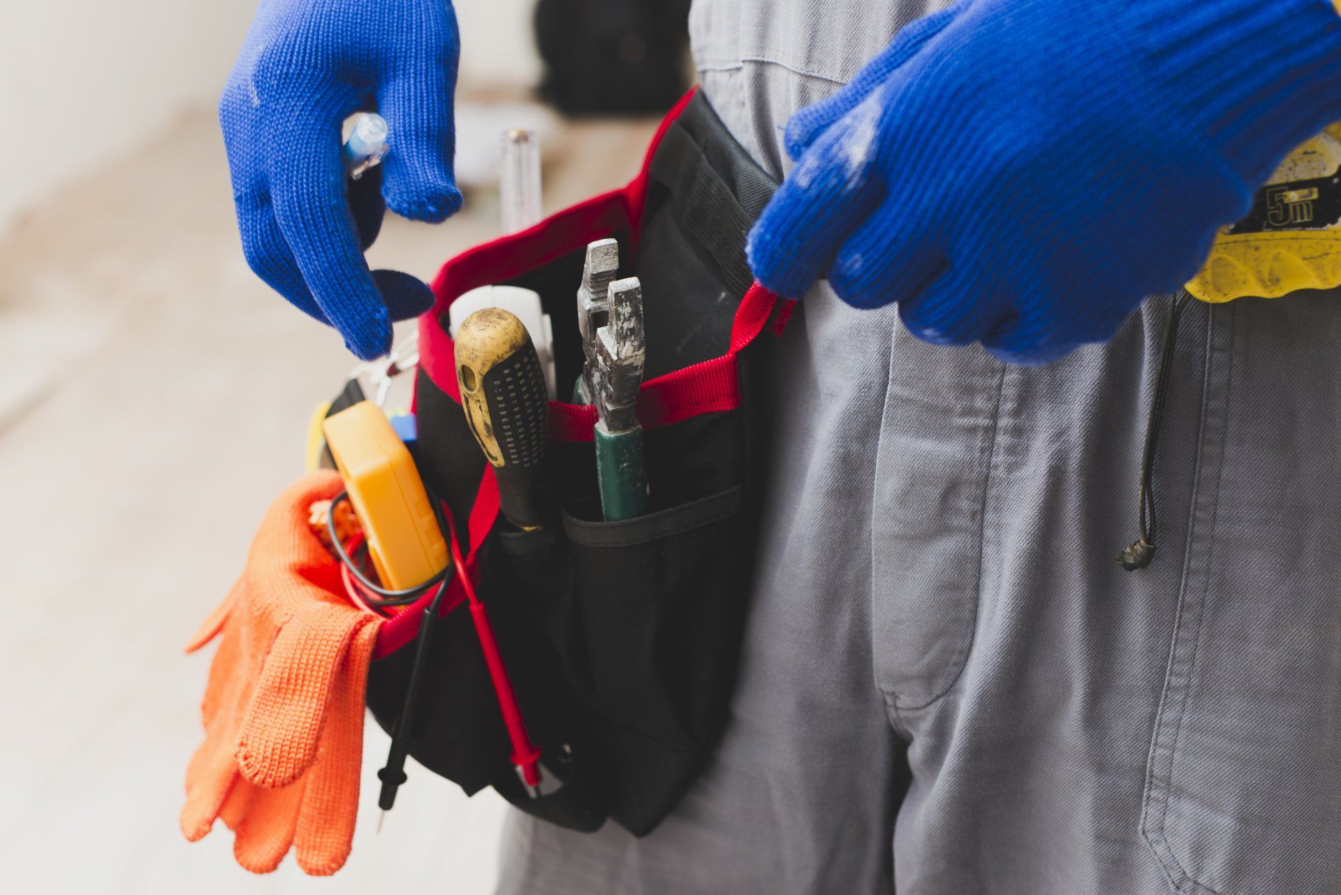 Person wearing blue gloves adjusts a red-and-black tool belt with tools and orange gloves attached