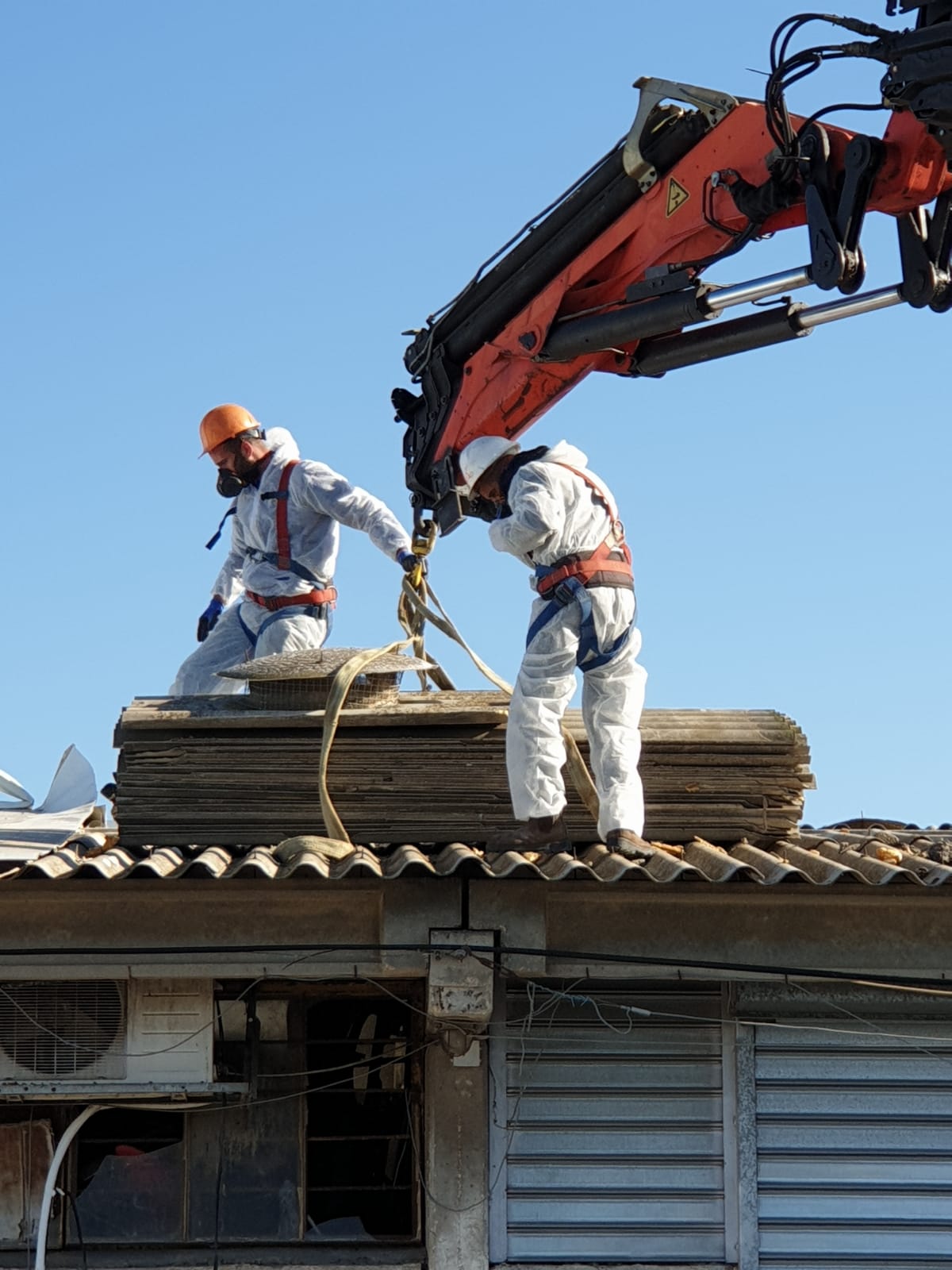 Construction workers on a roof using a crane to move materials against a blue sky