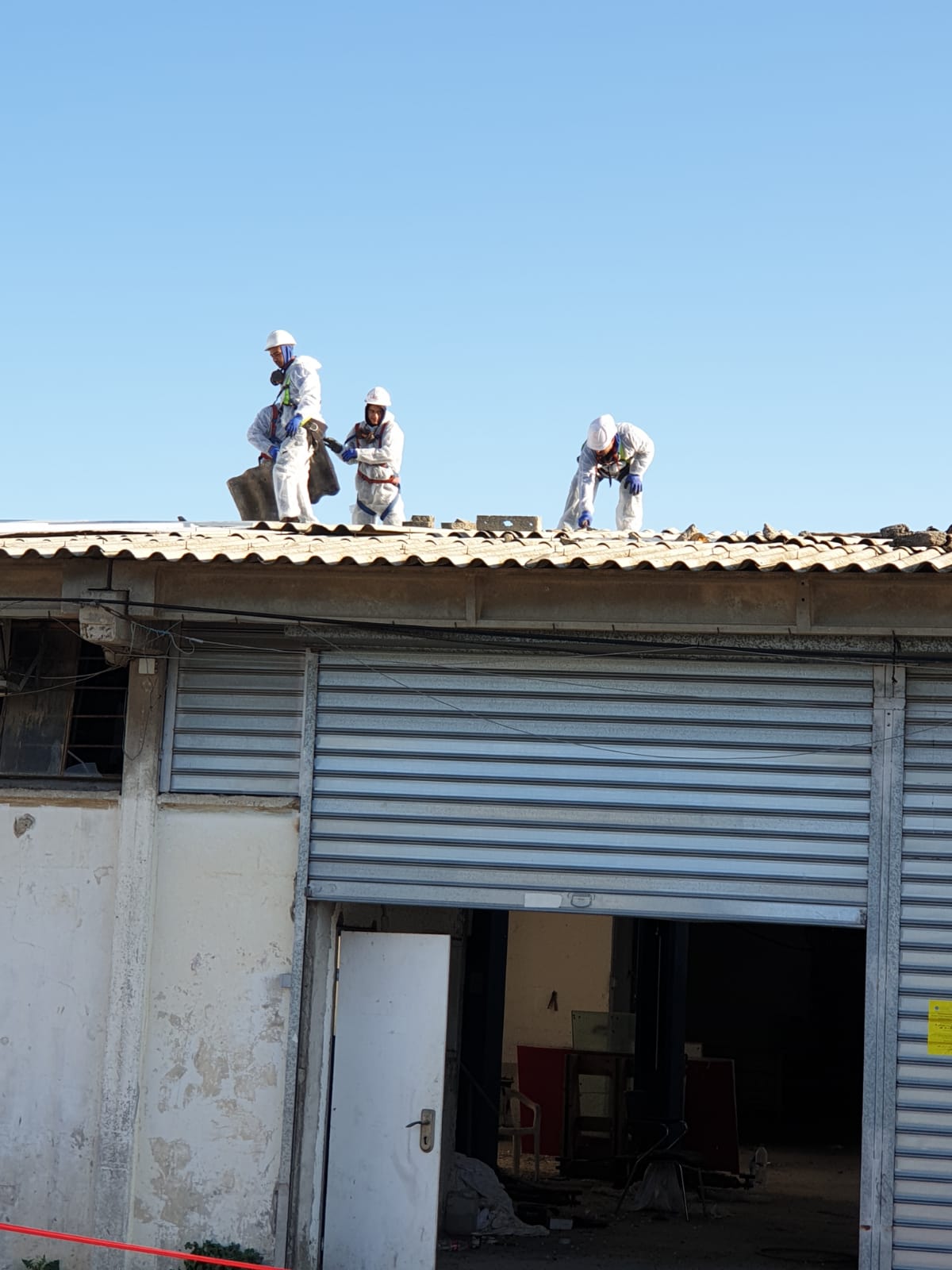 Workers on a corrugated roof repairing a building with an open garage door.