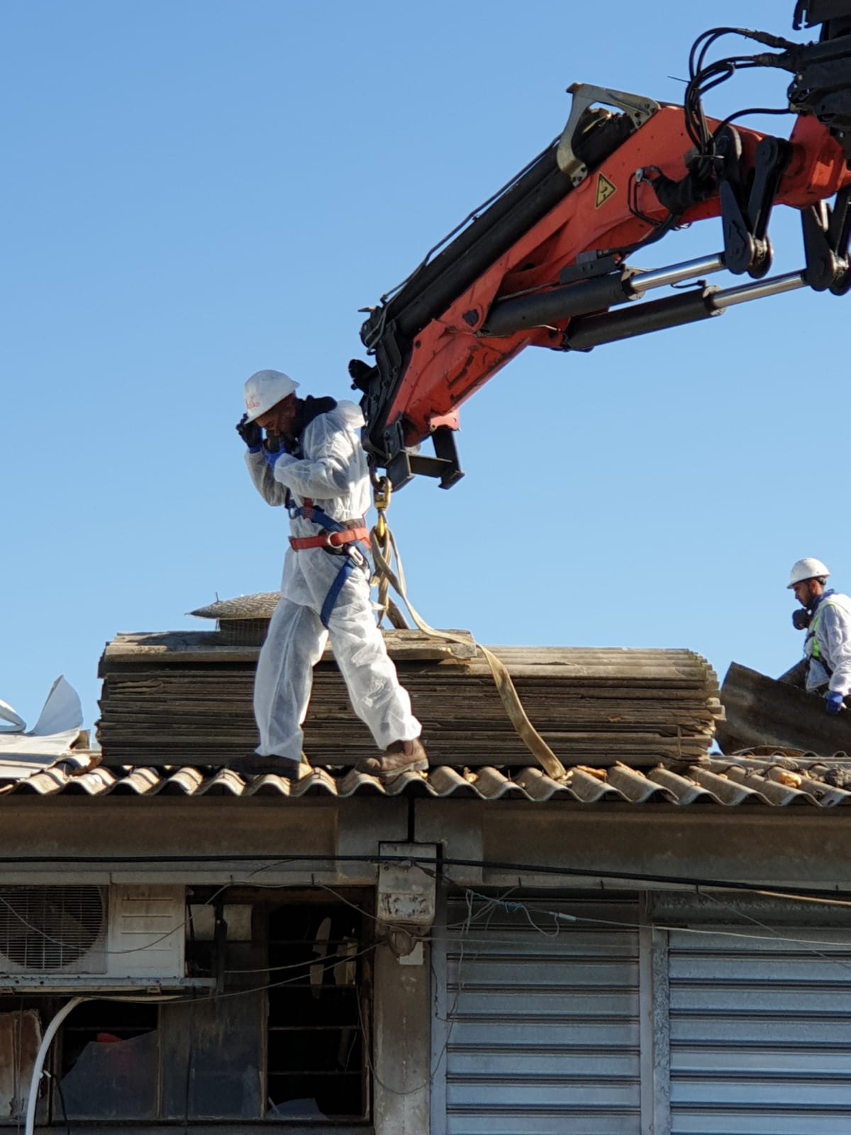 Construction workers repairing a roof with a red crane on a house under a blue sky