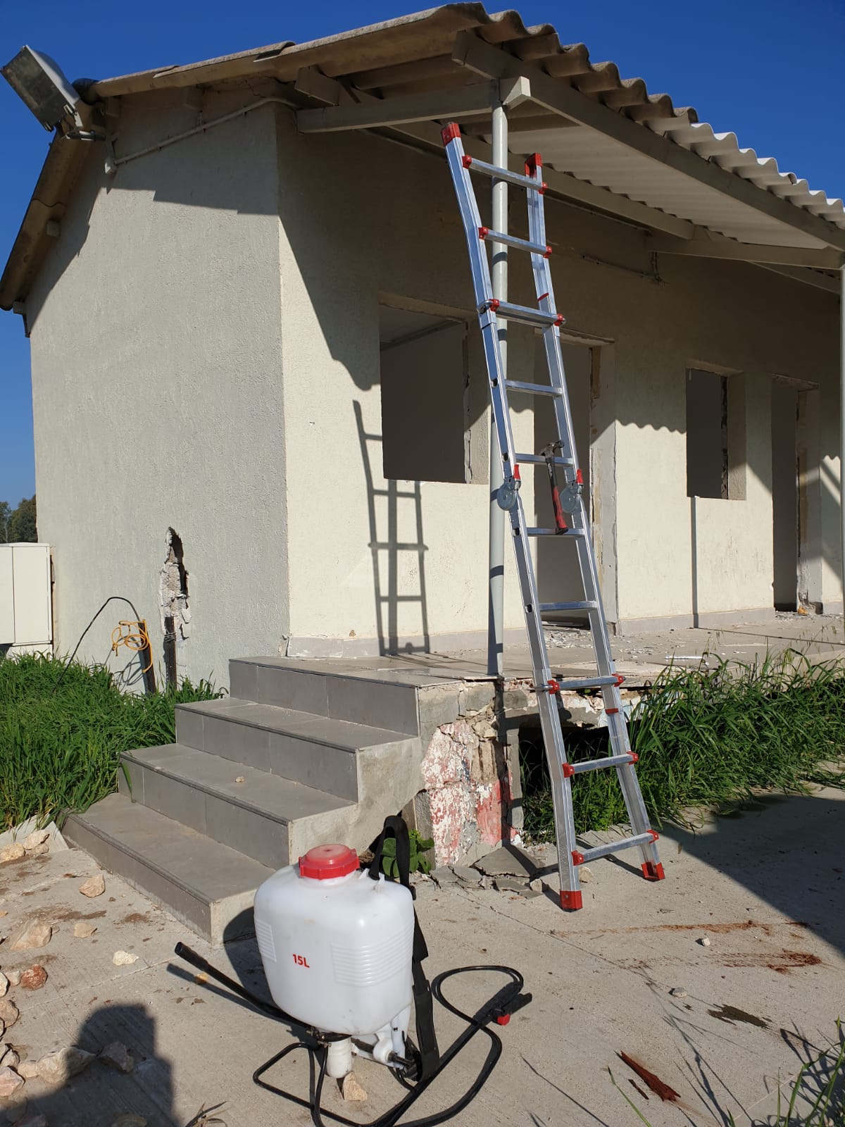 Ladder leaning against a stucco house with a asbestos roof paint sprayer on the ground and steps in front