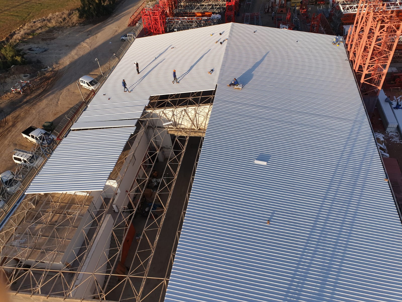 Aerial view of a large curved construction roof with concentric gray patterns and scaffolding around it.