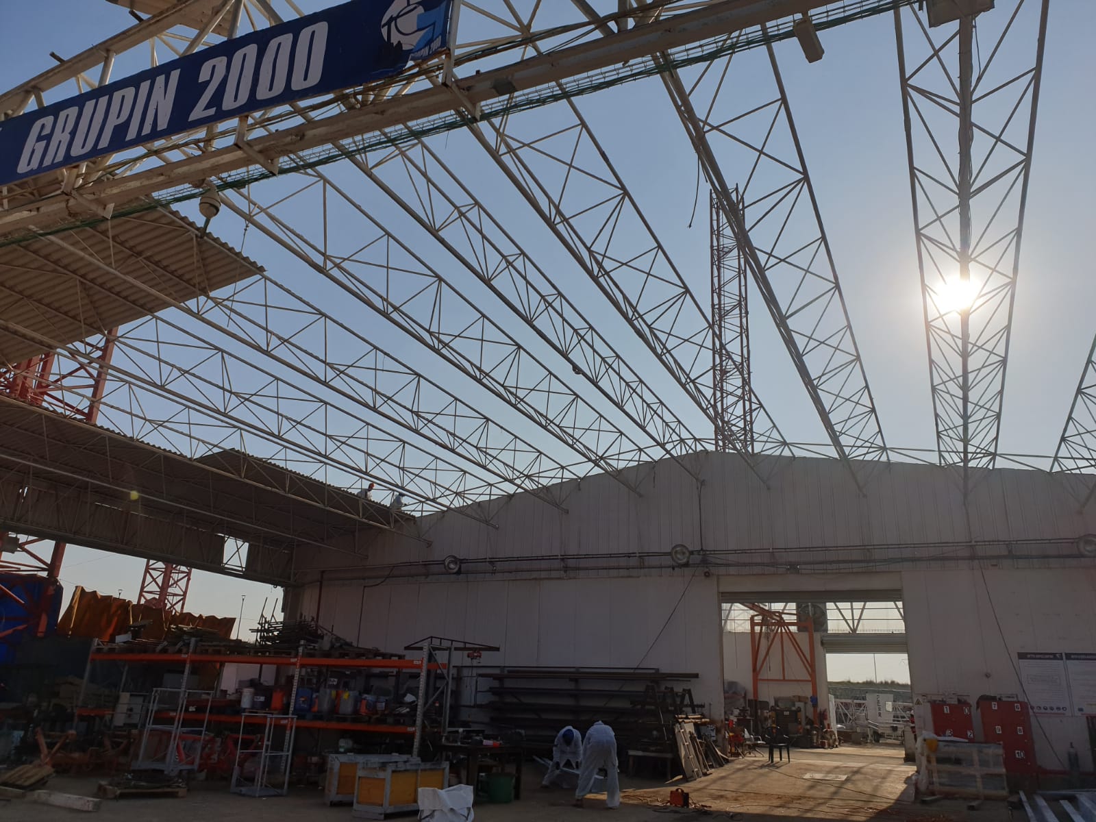 Construction site under a large steel canopy with workers, scaffolding, and bright sunlight overhead