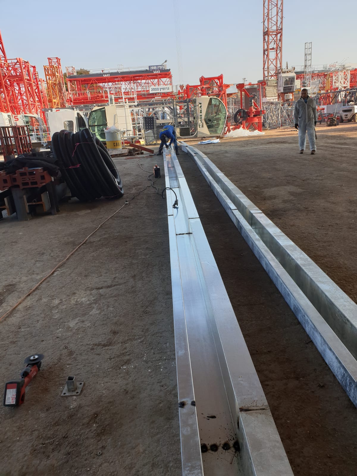Construction site with long metal beams laid on the ground and workers in the background