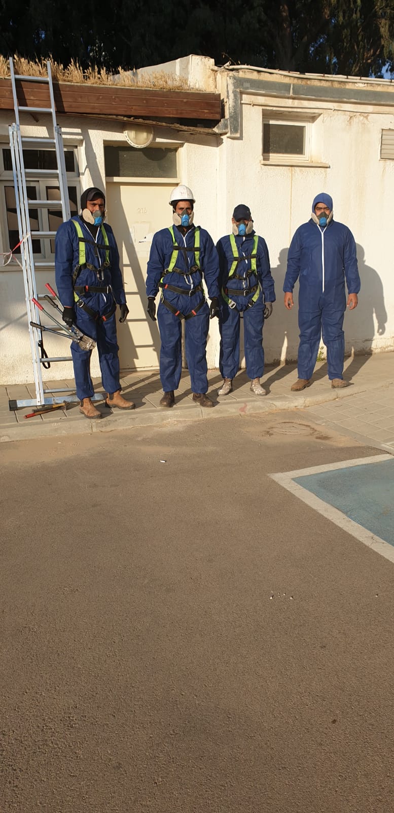 Four asbestos workers in blue uniforms standing outside a building by the roadside.