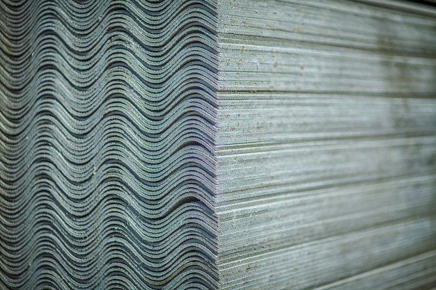 Close-up of stacked corrugated asbestos sheets with wavy edges and gray-green tones