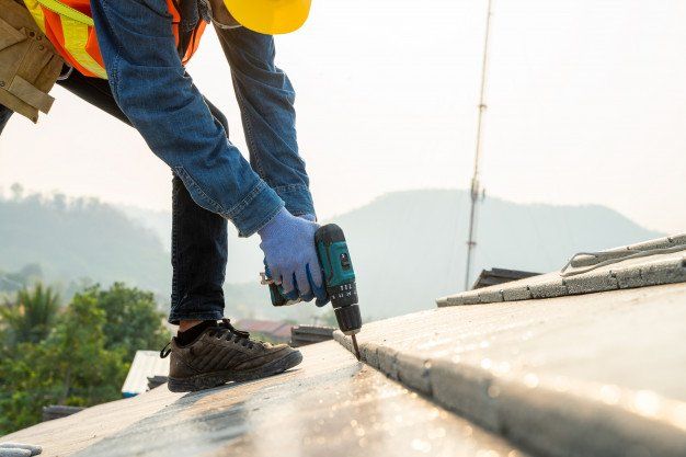 Worker using a drill to fasten metal roofing on a rooftop