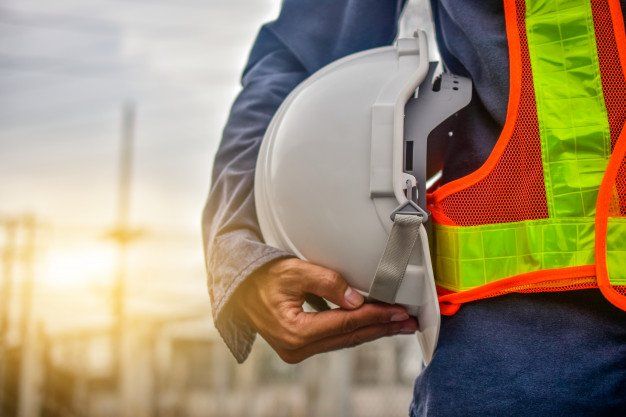 Construction worker holding a hard hat beside a neon safety vest at a worksite