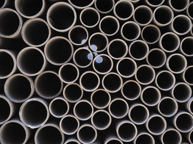 Stacked metal pipes viewed from the ends, forming a dense circular pattern with a small blue reflection