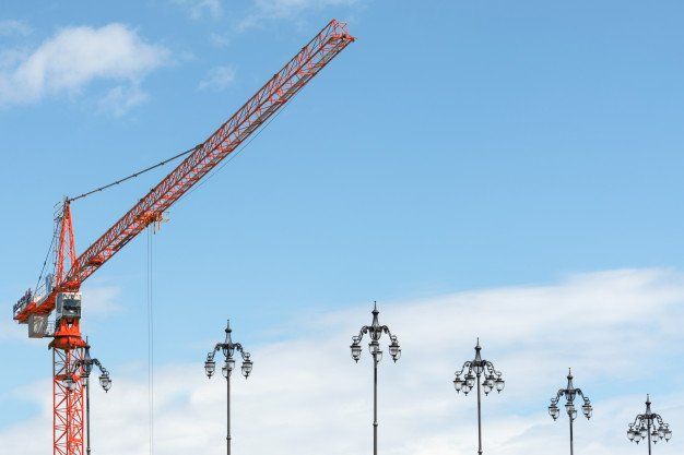 Red construction crane against a blue sky with decorative street lamps below