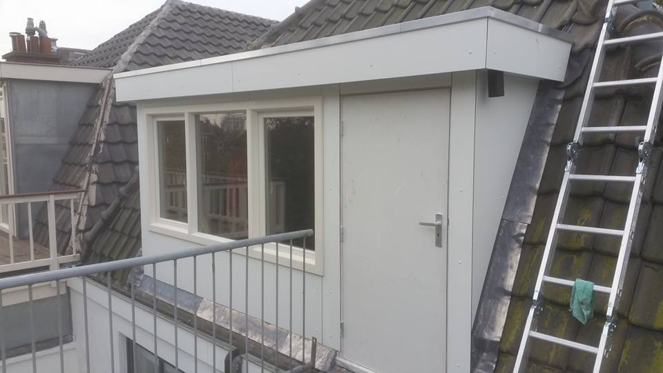 Een witte dakkapel met een raam en een deur, die uitkijkt op een balkon, met een ladder die tegen het dak leunt.