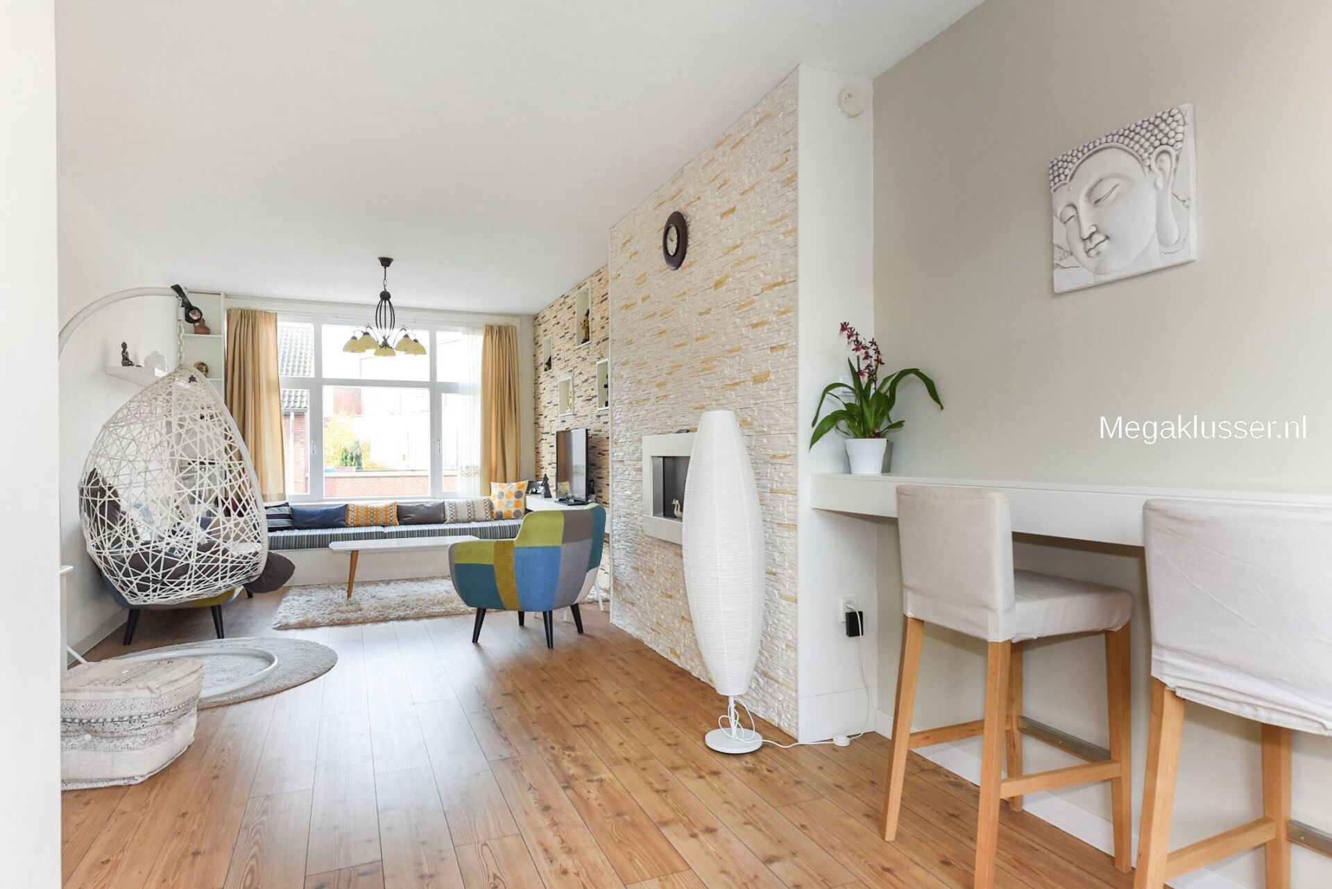 Een moderne woonkamer met houten vloeren, een bakstenen accentmuur, een hangende eierstoel en een ontbijtbar met hoge barkrukken.