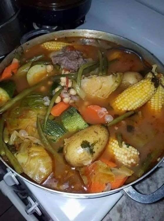 A pot of soup with vegetables and meat is on a stove.