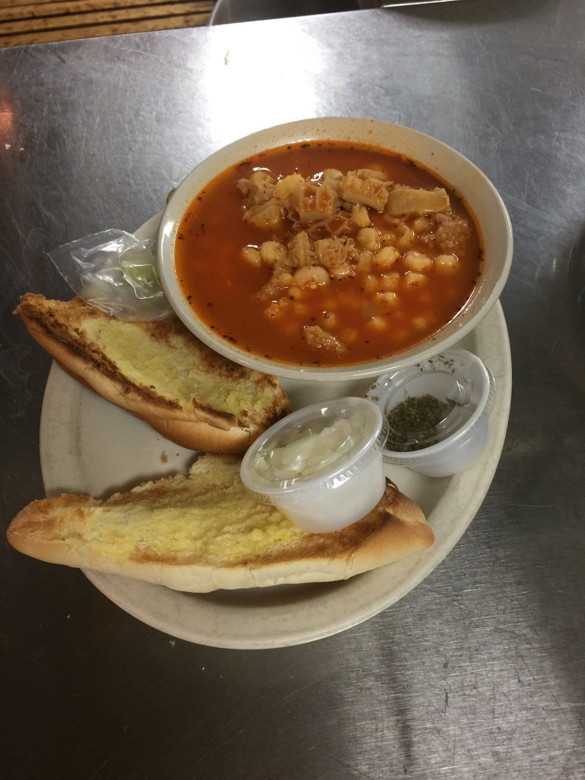 A bowl of soup with garlic bread and dipping sauce on a plate.
