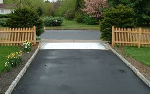 A black asphalt driveway with a wooden fence in the background.