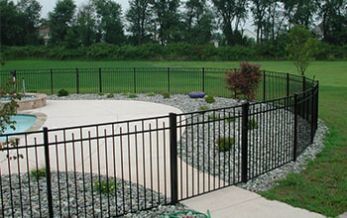 A black fence surrounds a swimming pool in a backyard.