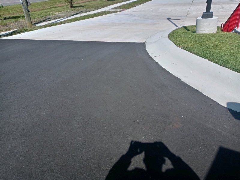 Curved suburban street with fresh black asphalt beside a light concrete sidewalk and grassy verge