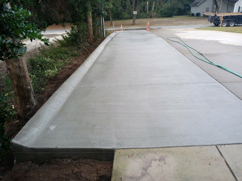 New concrete sidewalk beside a road with an orange cone and hose in the distance