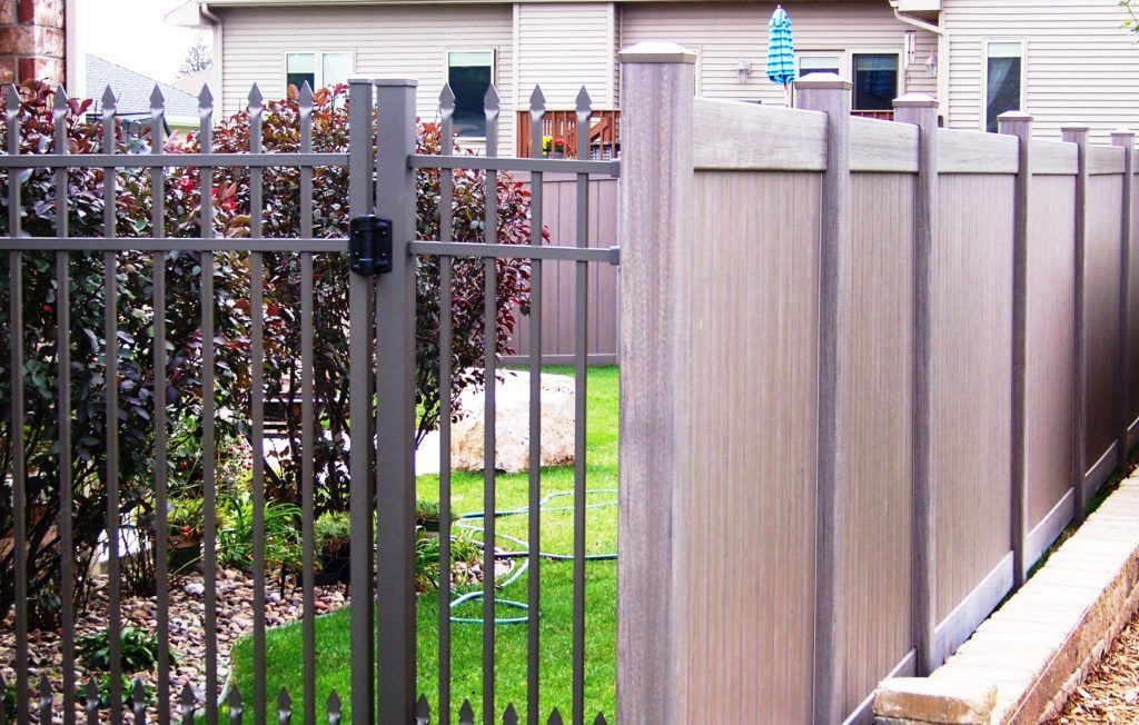 An aluminum fence meets a vinyl fence fence at the side of a yard