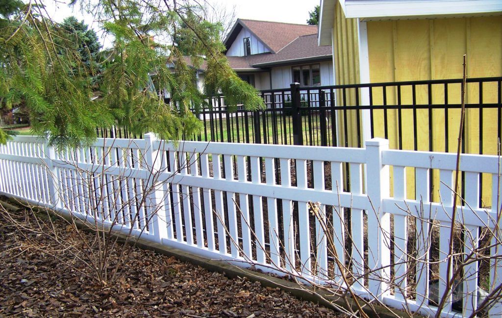 A white vinyl fence with a yellow house in the background