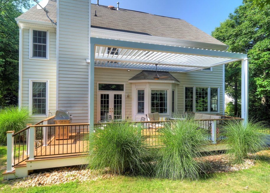 The back of a house with a large deck and a white motorized pergola.