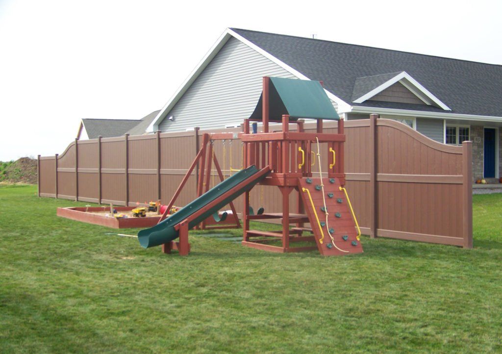A playground with a slide and brown vinyl fence in front of a house