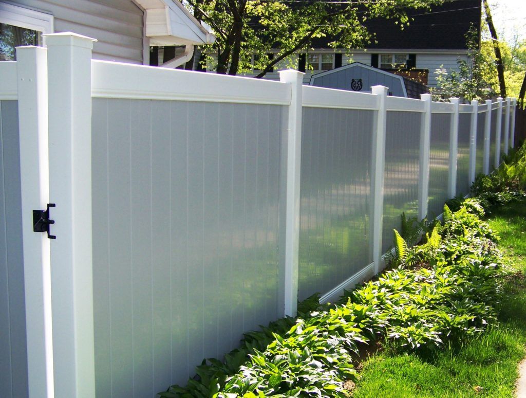 A vinyl fence surrounds a yard with a house in the background