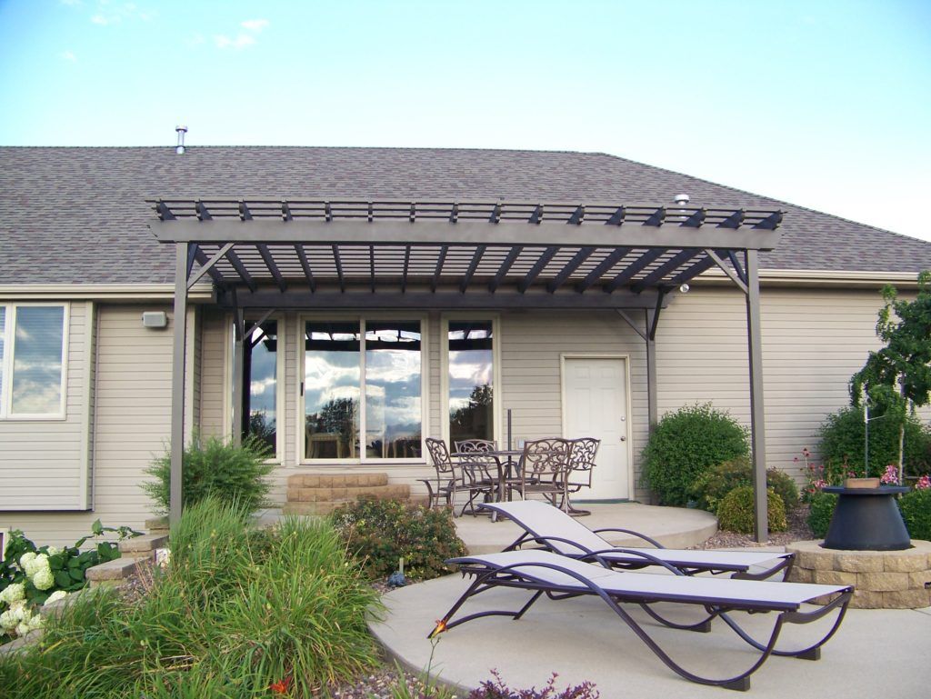 A house with a pergola and lawn chairs 