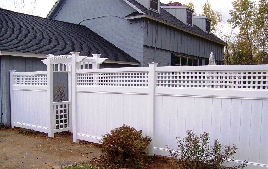 A white fence with an arbor and gate on the side of a house