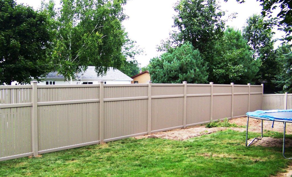 A trampoline is sitting in the grass next to a vinyl fence.