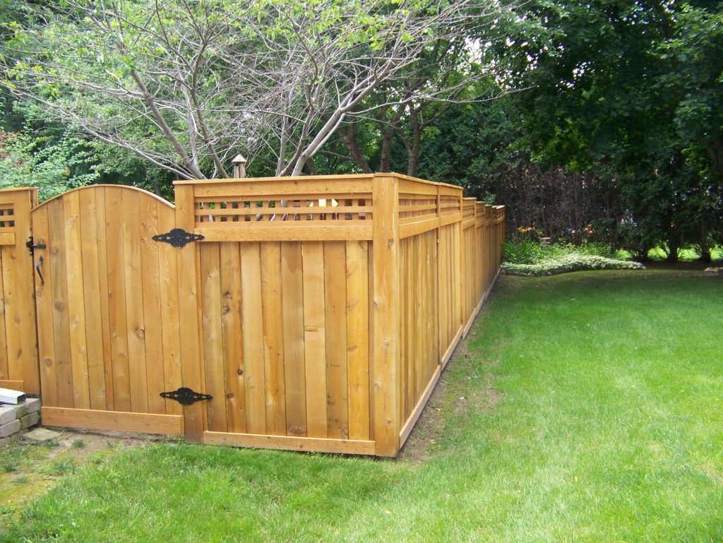 A wooden fence with a gate in a backyard surrounded by trees.