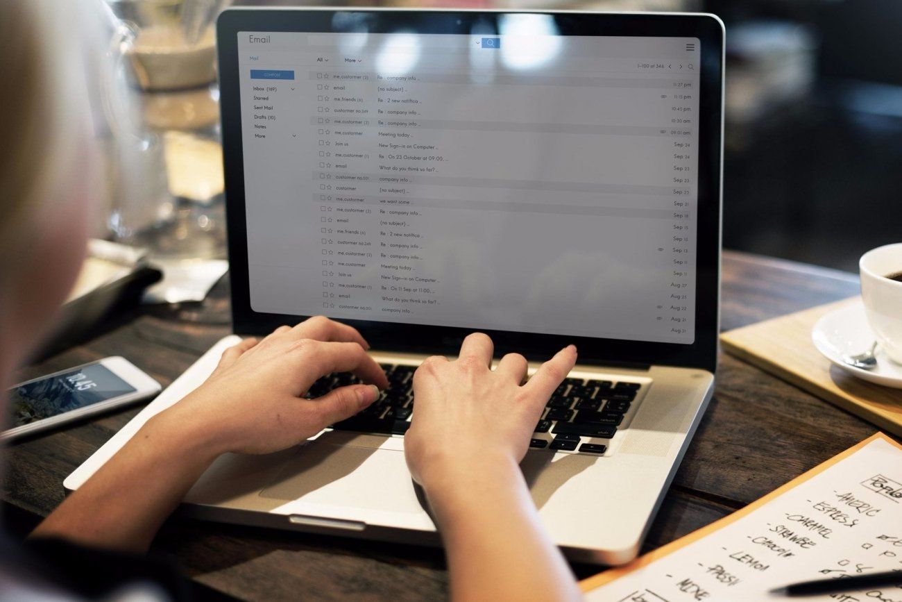 Person typing on a laptop at a table with coffee, a phone, and notes.