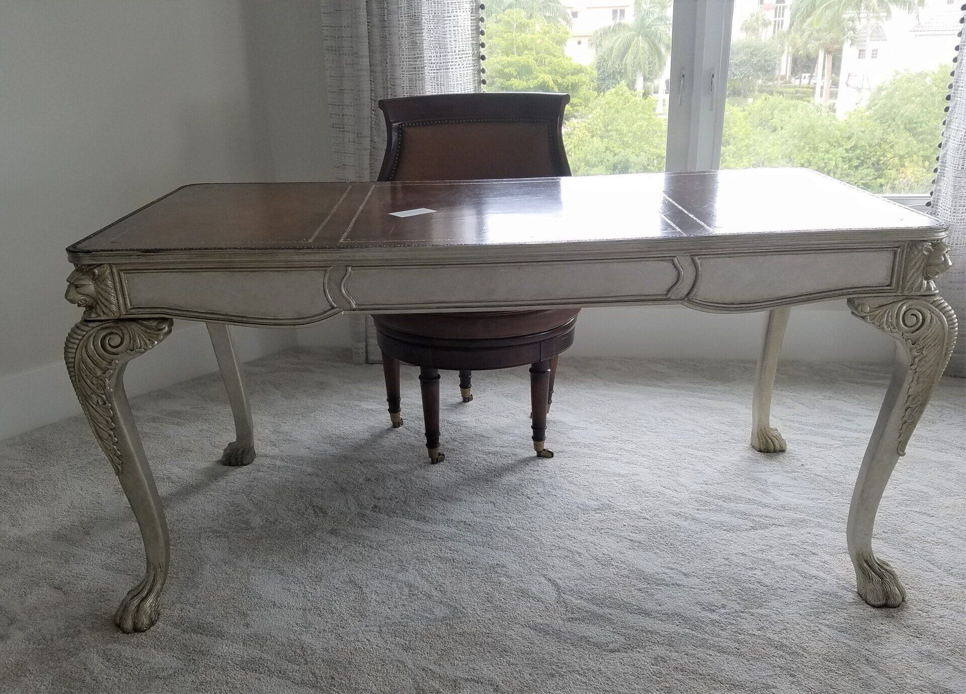 A wooden desk with ornate legs, a matching chair, and a window in the background.