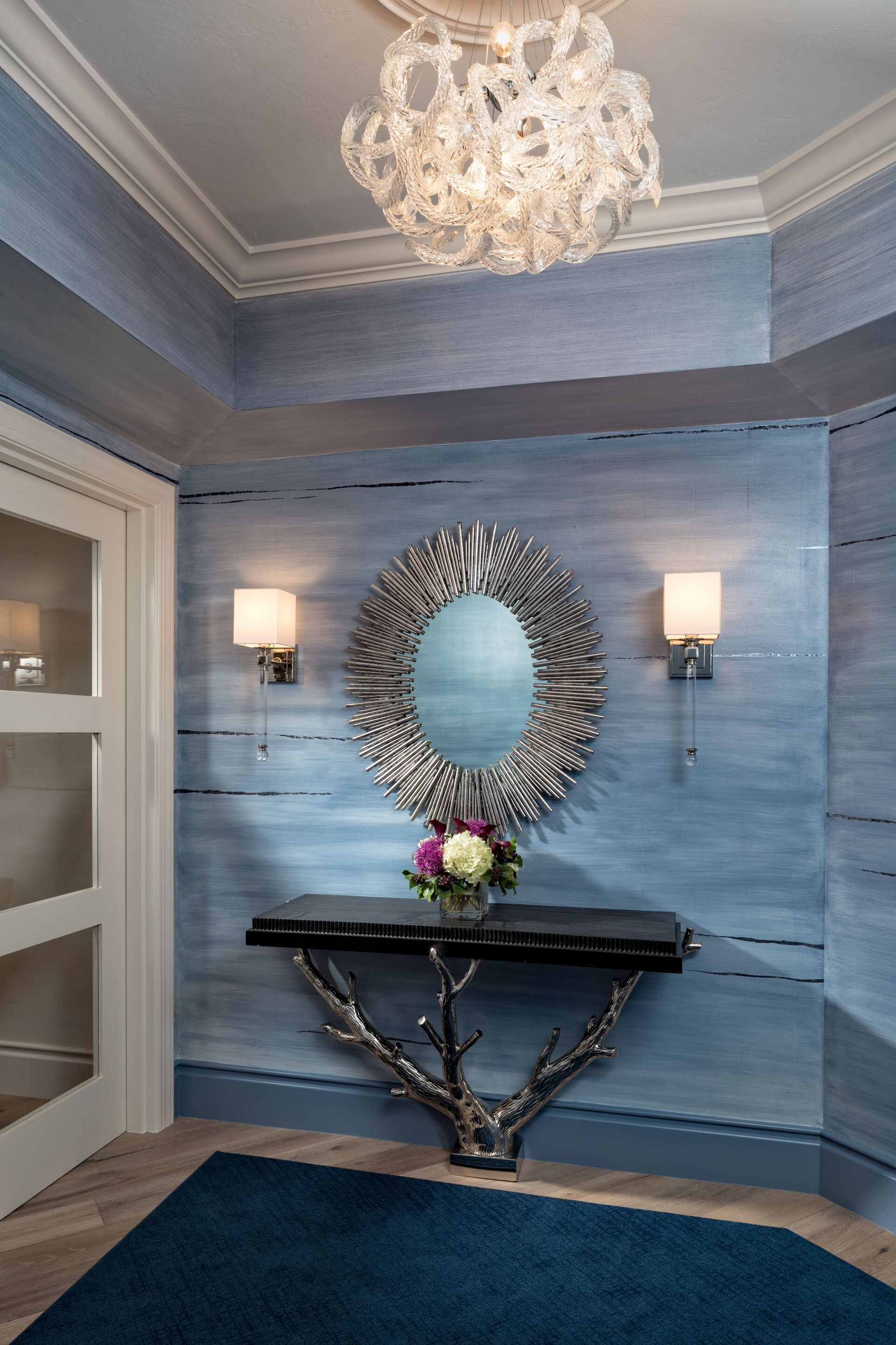 Blue entryway with a decorative mirror, sconces, and a console table.