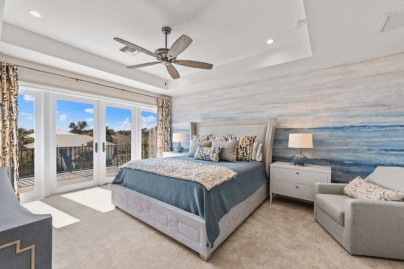 Bedroom with a bed, nightstand, chair, and ocean-themed accent wall. Large doors open to an outdoor deck.