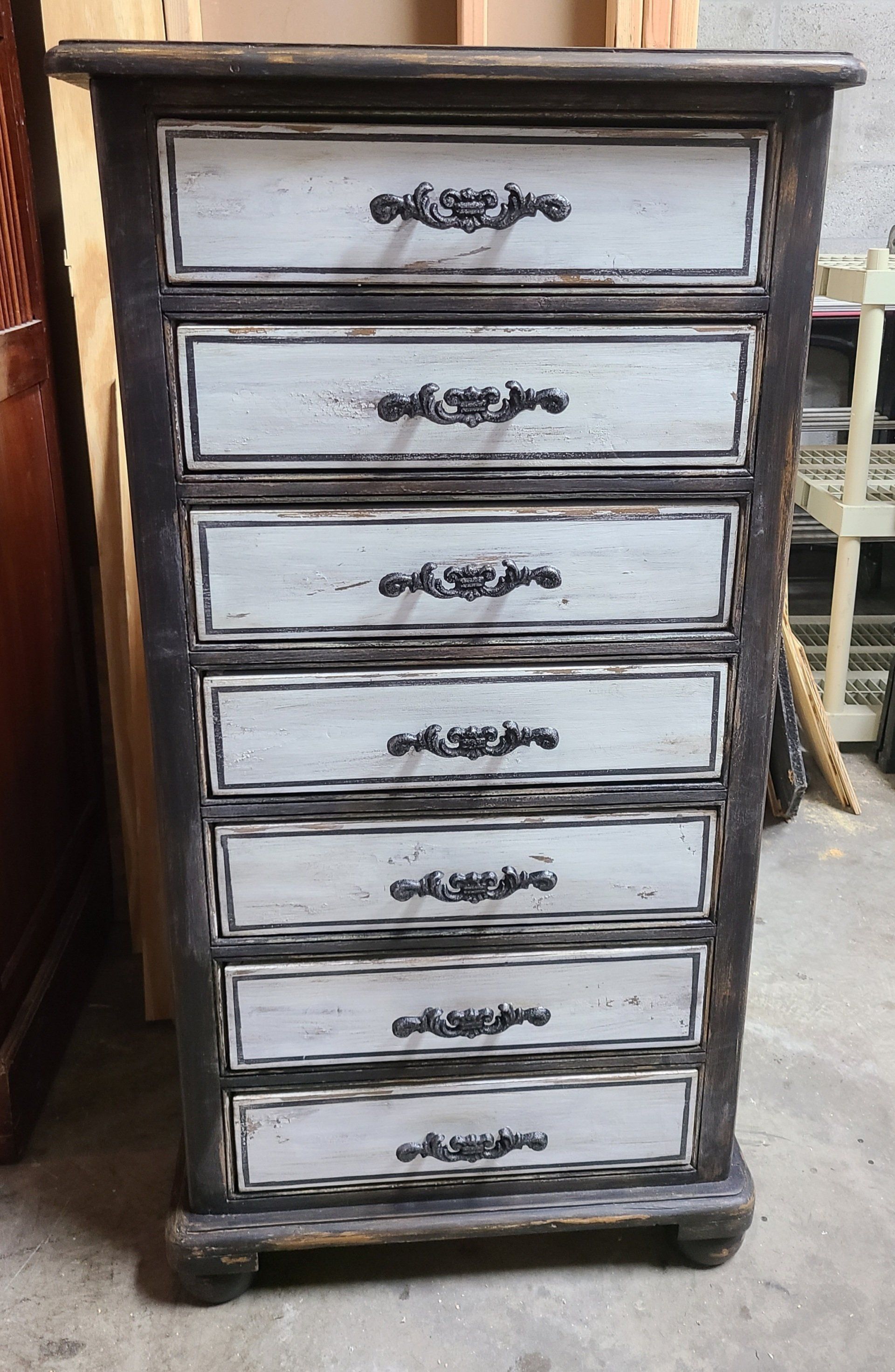 Tall, distressed wooden chest with seven drawers, gray and black color scheme.
