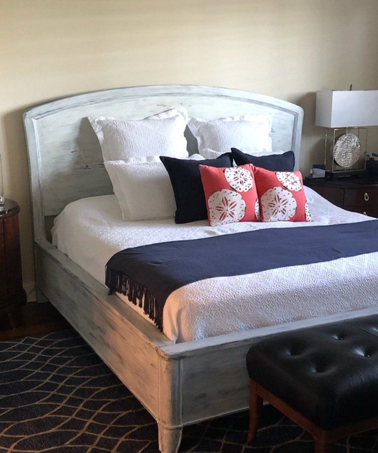 Bedroom with light blue distressed bed frame, white bedding, navy runner, and colorful pillows.