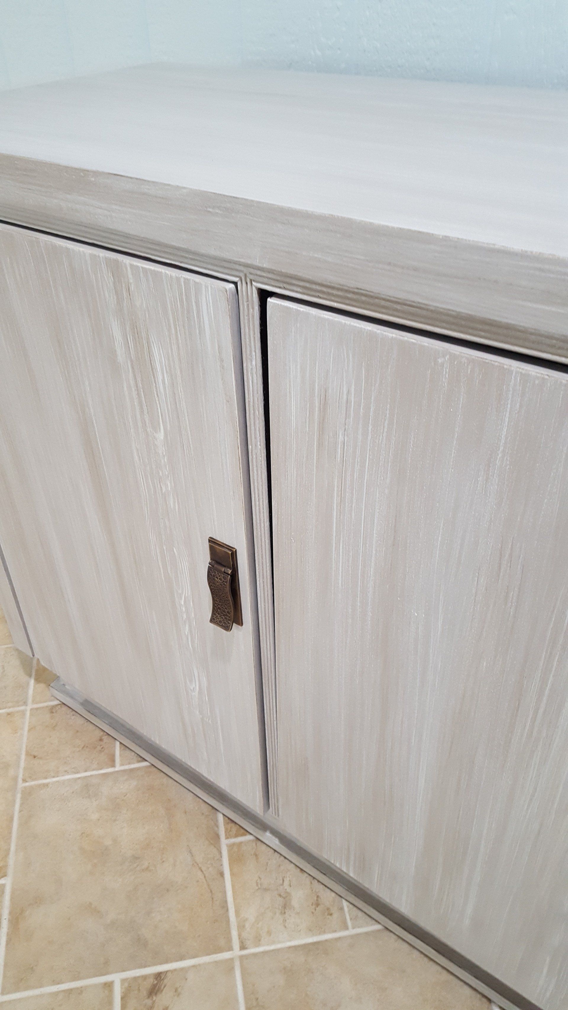 Wooden cabinet with light gray, textured doors and a dark, ornate handle.