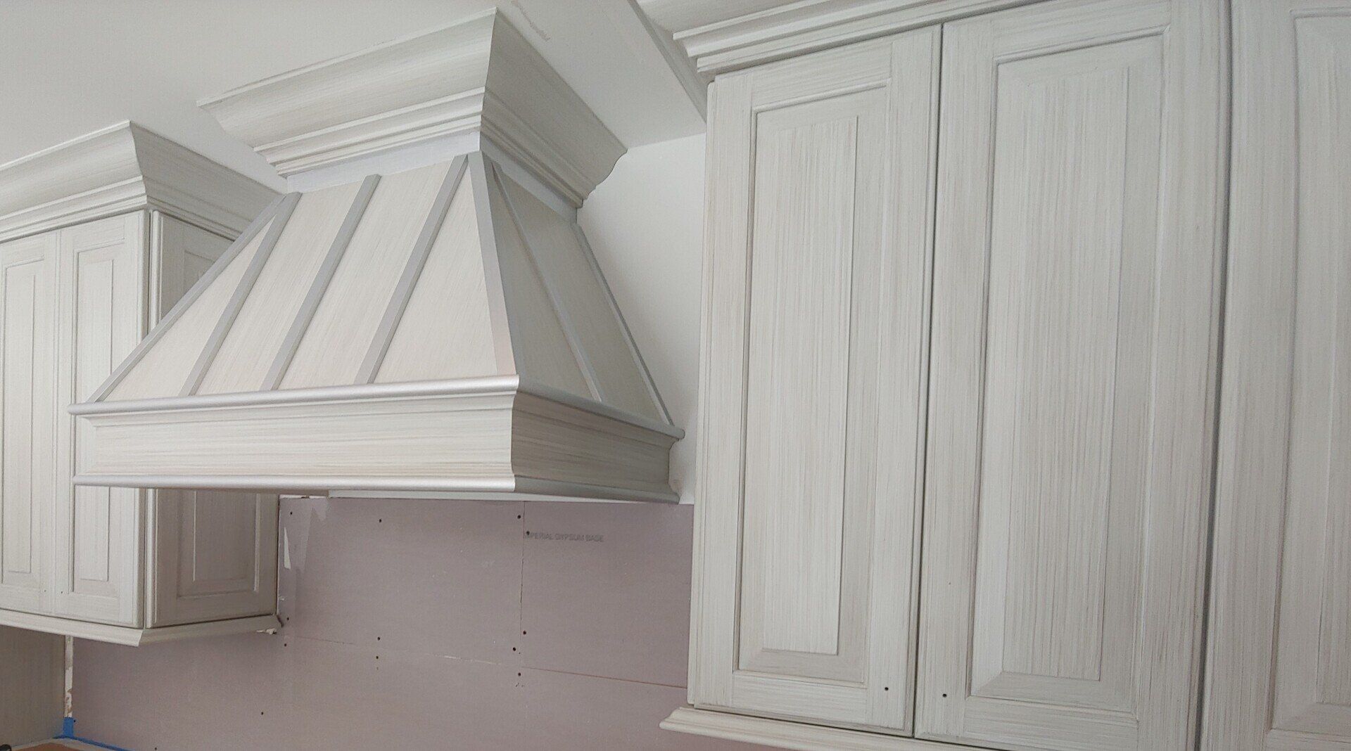White kitchen cabinets and range hood with a distressed, aged finish.