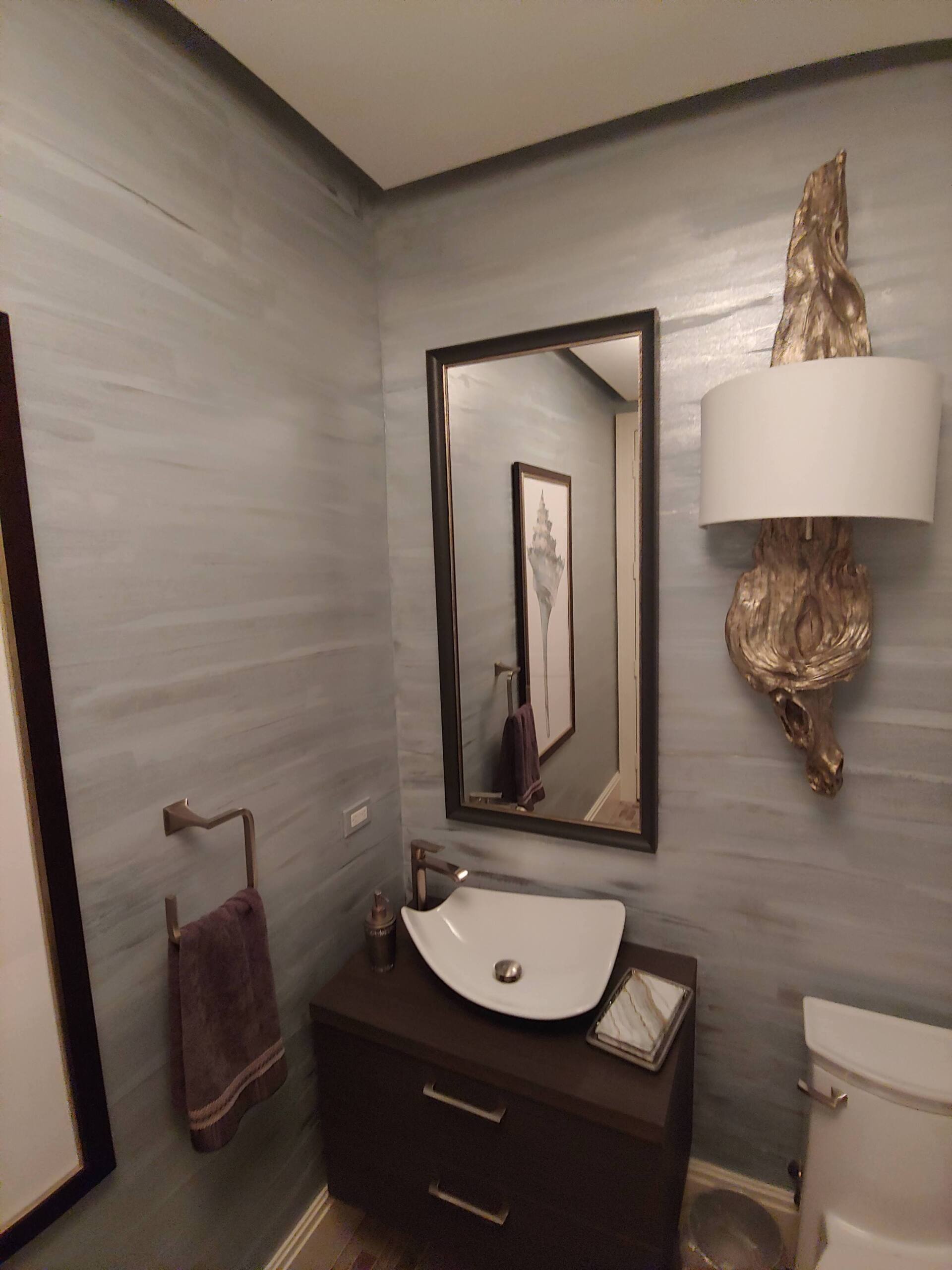 Small bathroom with gray walls, dark vanity, white sink, and ornate gold sconce.